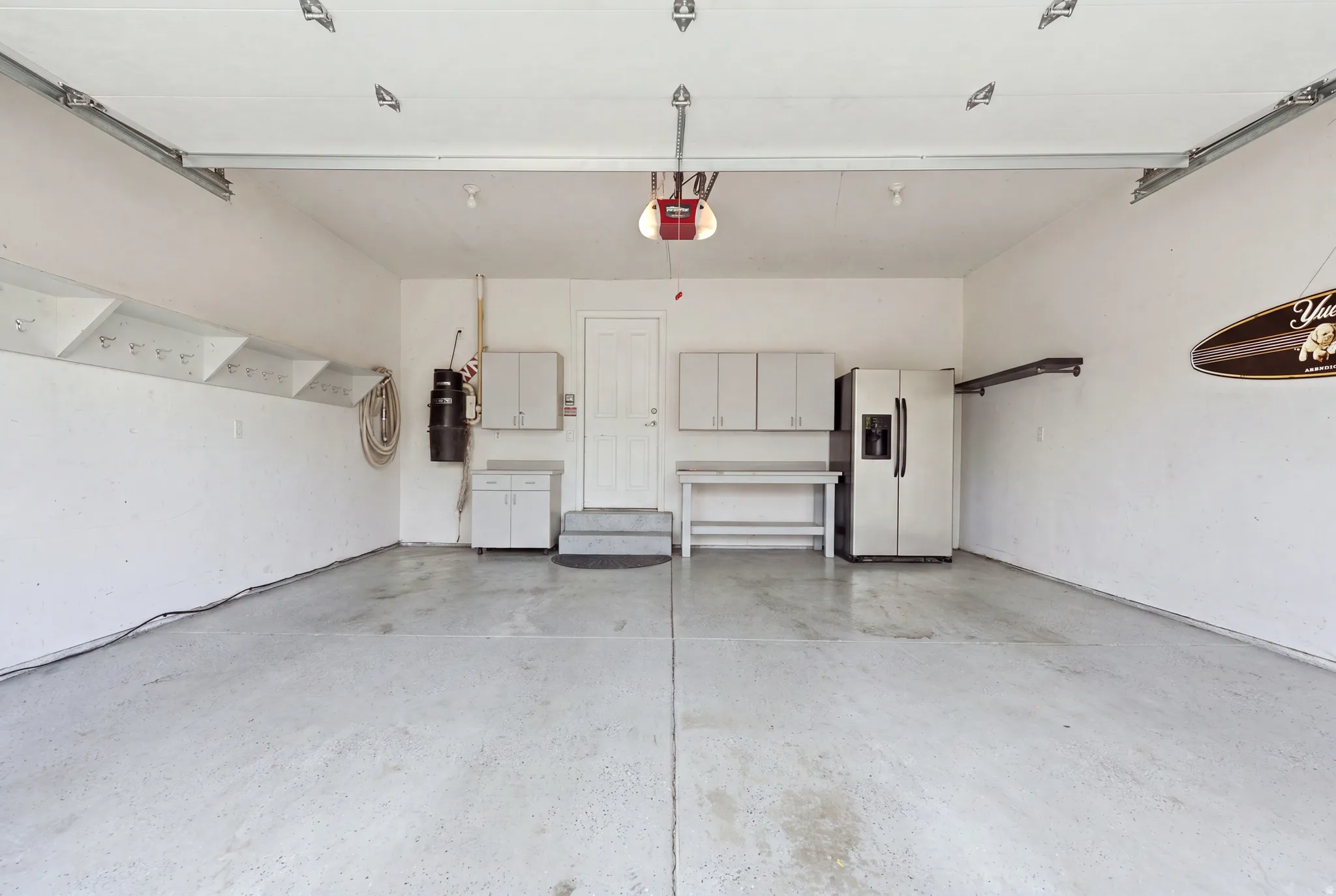 Spacious garage featuring a durable concrete floor, an overhead garage door, built-in shelving, and white cabinetry