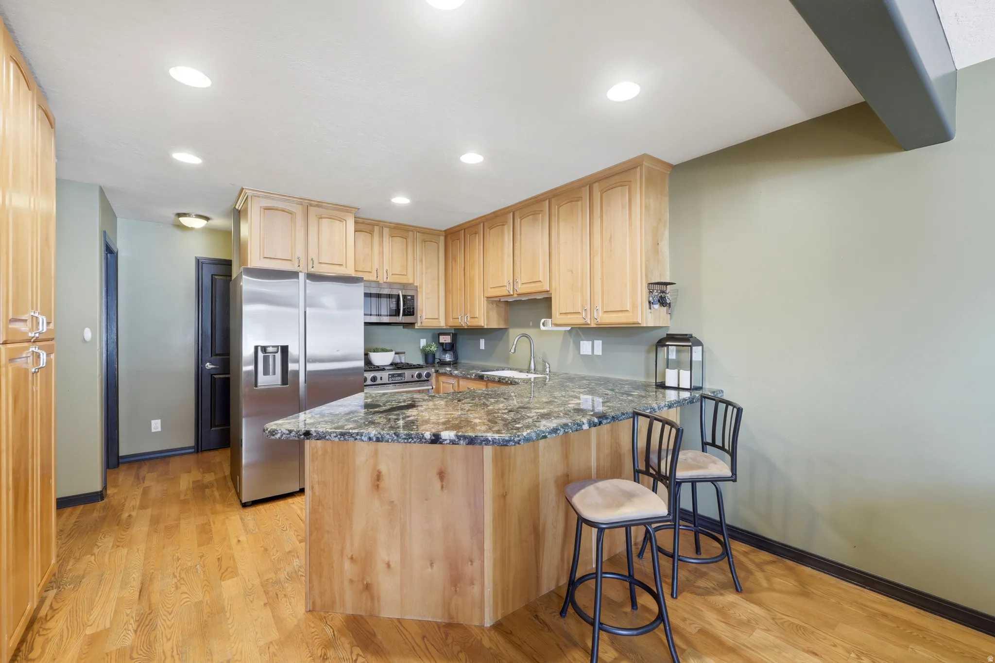 Full kitchen featuring wood-finish cabinetry, stainless steel appliances, granite-patterned countertops, and recessed lighting