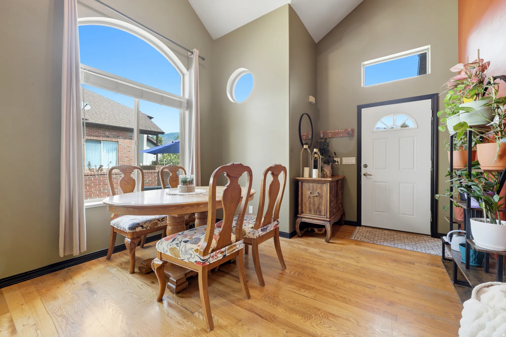 Dining area featuring high ceilings, hardwood flooring, an arched picture window, a circular accent window, and a white front entry door with a transom window