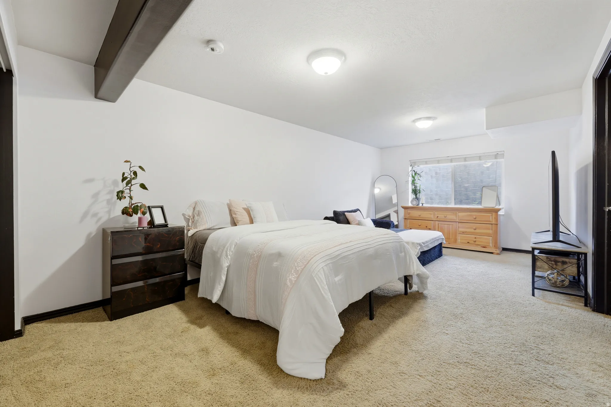 Spacious room with plush carpeting, prominent exposed ceiling beam, recessed lighting, and a large window