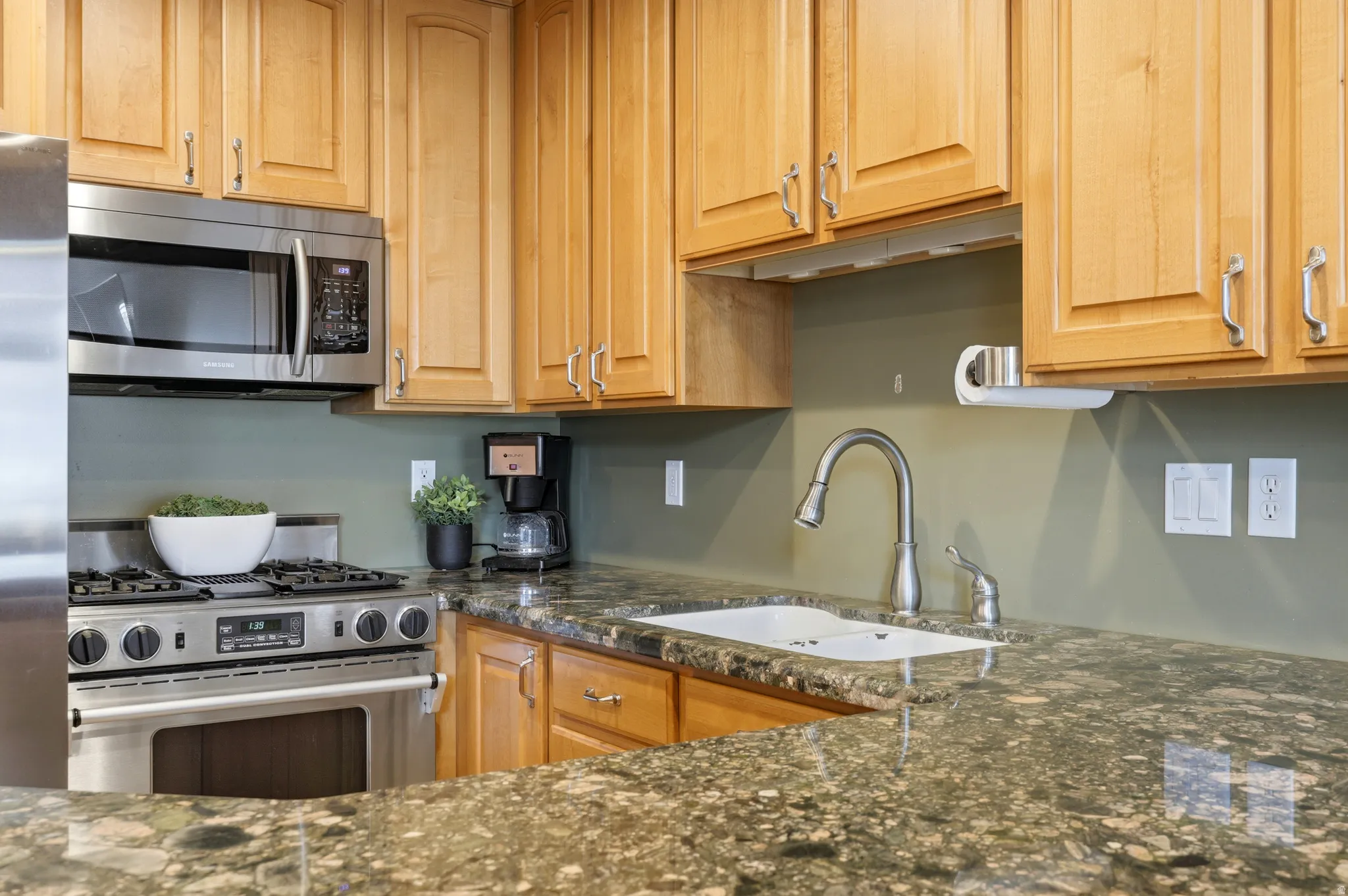 Kitchen featuring granite countertops, wood cabinetry, stainless steel appliances, an undermount sink, and a gooseneck faucet