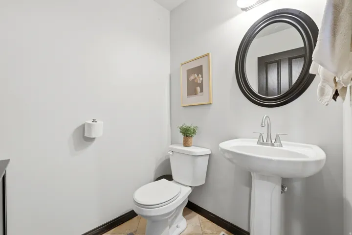 Pedestal sink with chrome faucet, circular framed mirror, and light gray wall paint