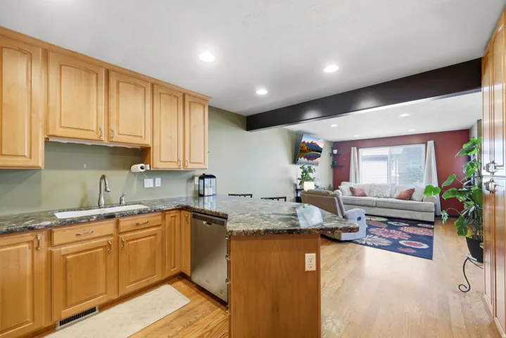Kitchen featuring light wood cabinetry, granite countertops, an undermount sink with a gooseneck faucet, and stainless steel dishwasher