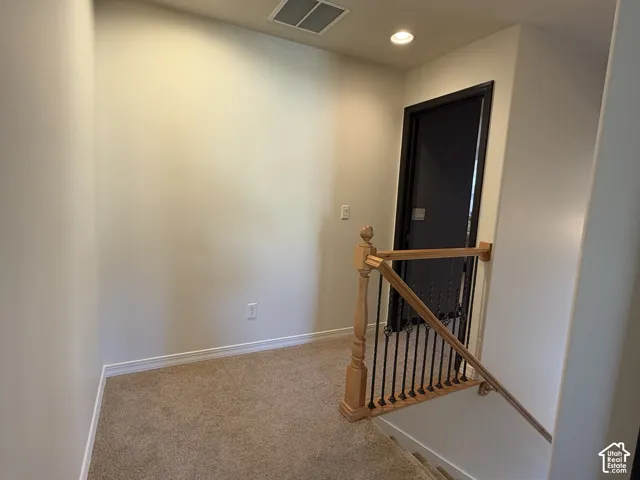Landing area featuring neutral carpet flooring, recessed lighting, and a wood handrail with metal balusters