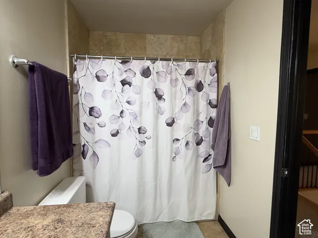 Bathroom featuring a shower surround tiled in neutral stone, a stone-finish countertop, and a wall-mounted metal towel rack