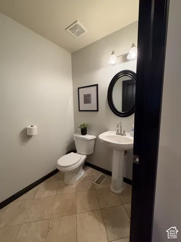 Powder room featuring a porcelain pedestal sink, oval wall-mounted mirror, dual-light vanity fixture, and diagonal-set tile flooring