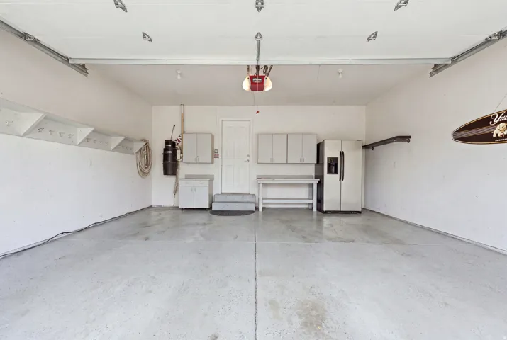 Spacious garage featuring a durable concrete floor, an overhead garage door, built-in shelving, and white cabinetry