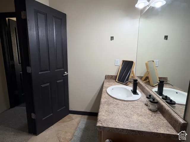 Vanity featuring a stone-look laminate countertop, an integrated white oval basin, and a matte black faucet, complemented by a large wall-mounted mirror, overhead lighting, and a dark-finish interior door