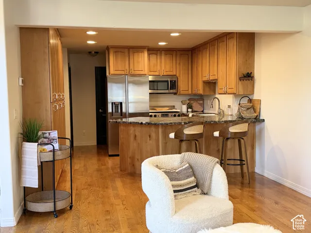 Kitchen featuring solid wood cabinetry, stone-surface breakfast bar, stainless steel appliances, and wood-finish flooring