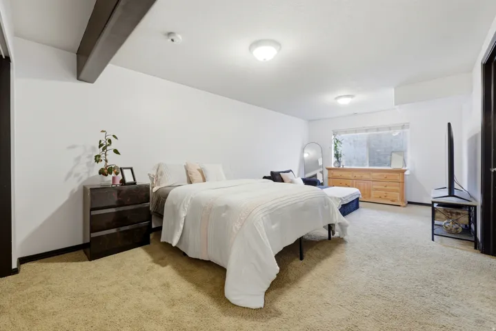 Spacious room with plush carpeting, prominent exposed ceiling beam, recessed lighting, and a large window