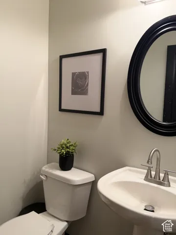 Pedestal sink with a dual-handle metal faucet, oval mirror with a black frame, and a white toilet