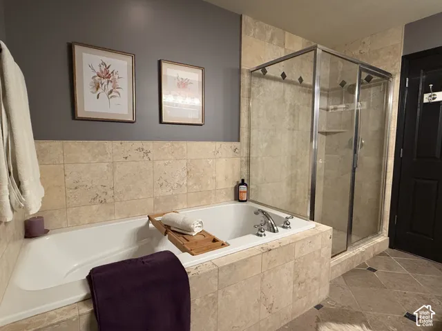 Soaking tub with a tiled surround, glass-enclosed shower, stone-finish tile flooring, and dark-toned wall paint
