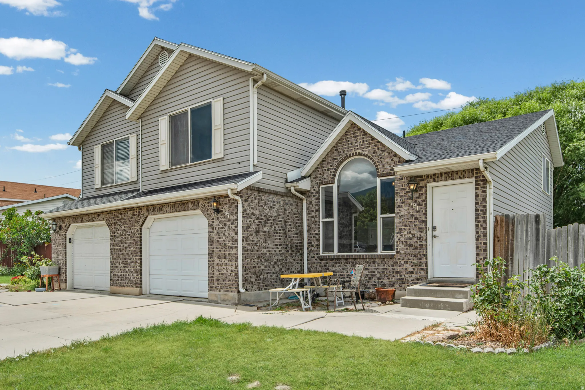 Two-story exterior featuring a brick and siding facade, a two-car garage, an arched window, and a white entry door