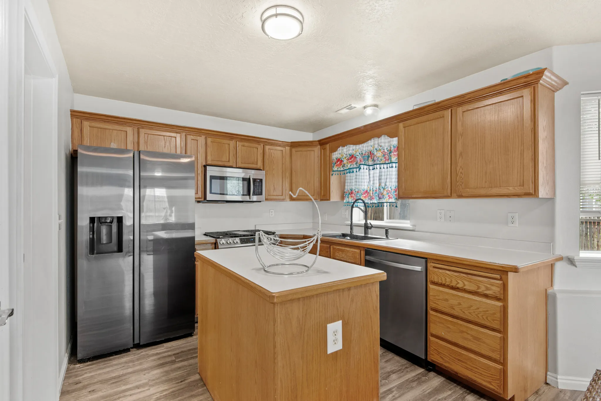Kitchen featuring wood cabinetry, white countertops, a central island, stainless steel appliances, and wood-finish flooring