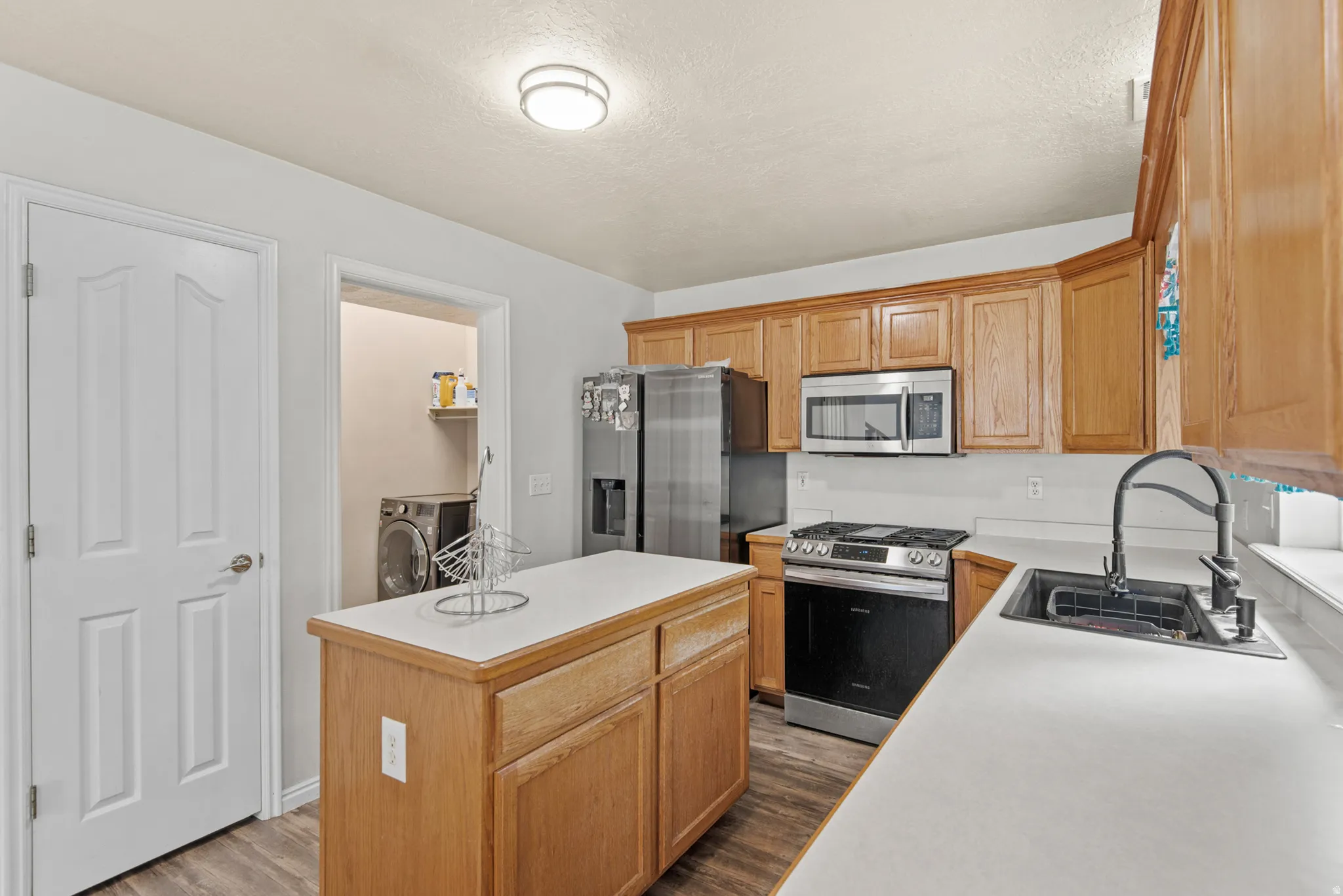 Kitchen featuring wood cabinetry, stainless steel appliances, a center island with countertop, and a black sink with a gooseneck faucet