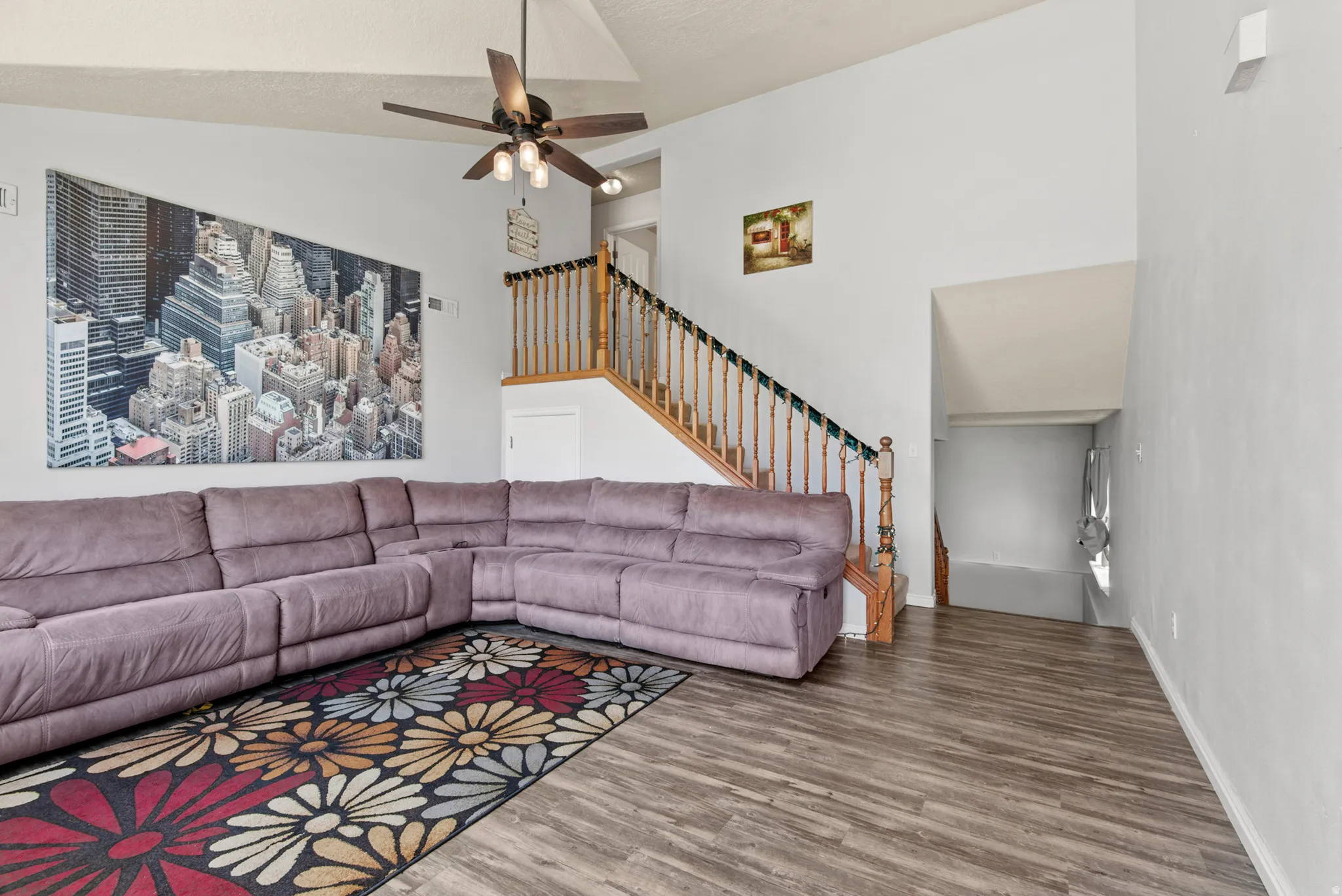 Vaulted ceiling with a ceiling fan, hardwood-look flooring, and a staircase featuring wood balusters
