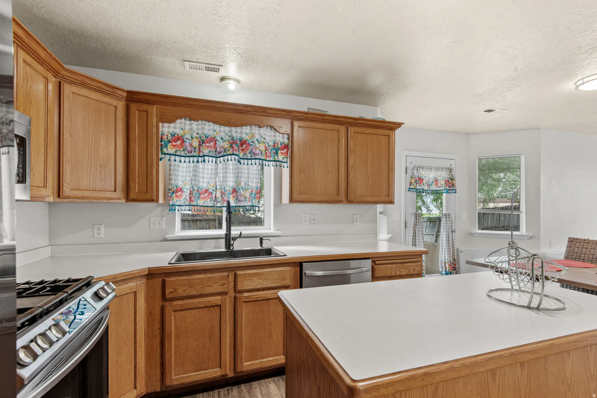 Kitchen featuring wood cabinetry, light countertops, stainless steel appliances, and a central island