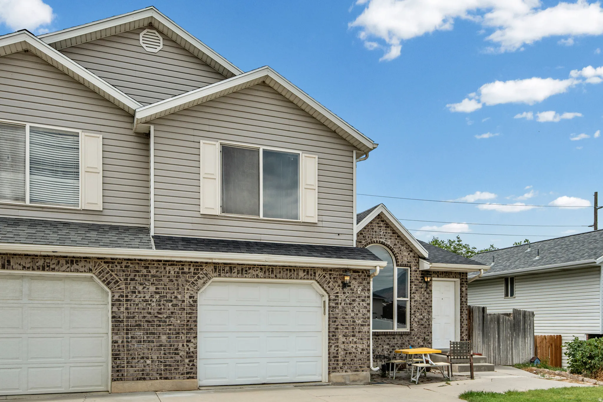 Exterior featuring light gray horizontal siding, brick veneer accents, dual attached garages, a prominent arched window, and a white entry door