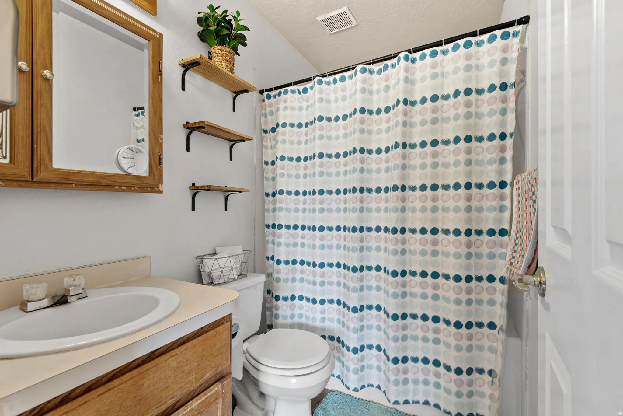 Bathroom featuring a vanity with a laminate countertop and undermount sink, wood-finish medicine cabinet, and three wall-mounted wood-finish shelves with black metal brackets