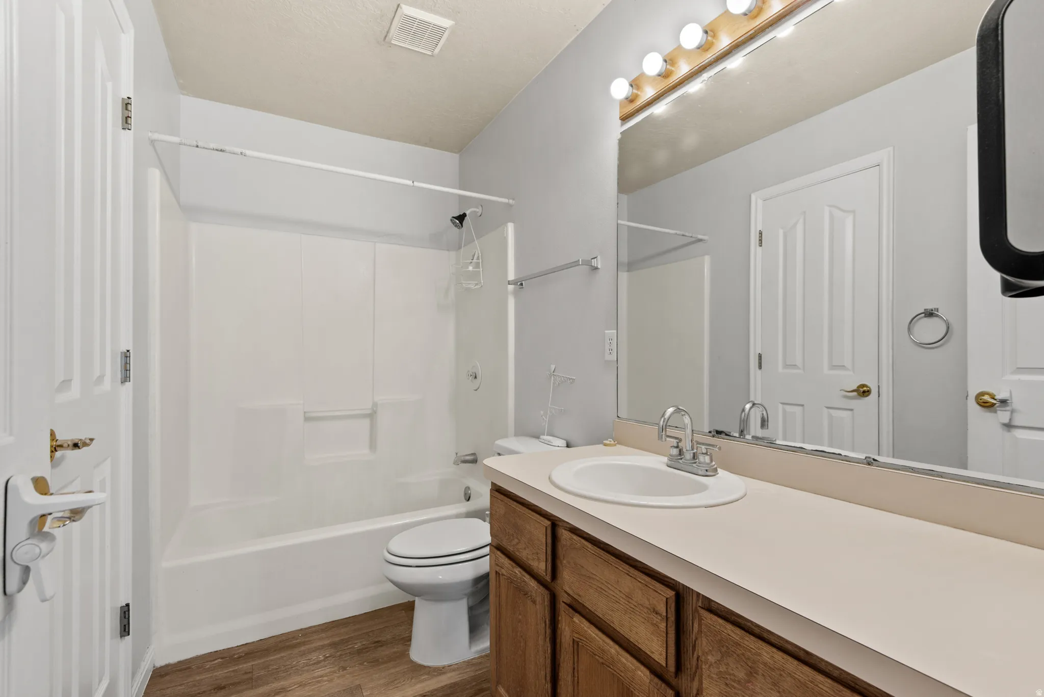 Full bathroom featuring a white tub and shower combination, wood-finish flooring, a vanity with wood cabinetry, a light-toned countertop, and a large mirror