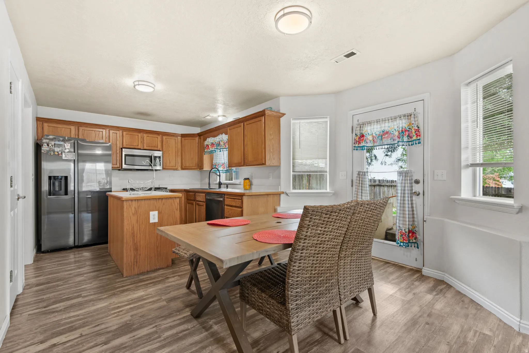 Kitchen and dining area featuring wood-finish flooring, light wood cabinetry, white subway tile backsplash, stainless steel appliances, and an eat-in island