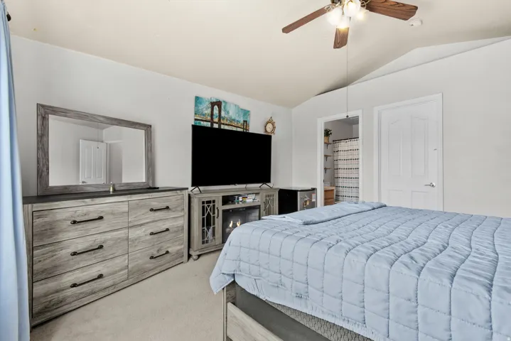Vaulted ceiling with a ceiling fan, carpet flooring, and a private bath entry