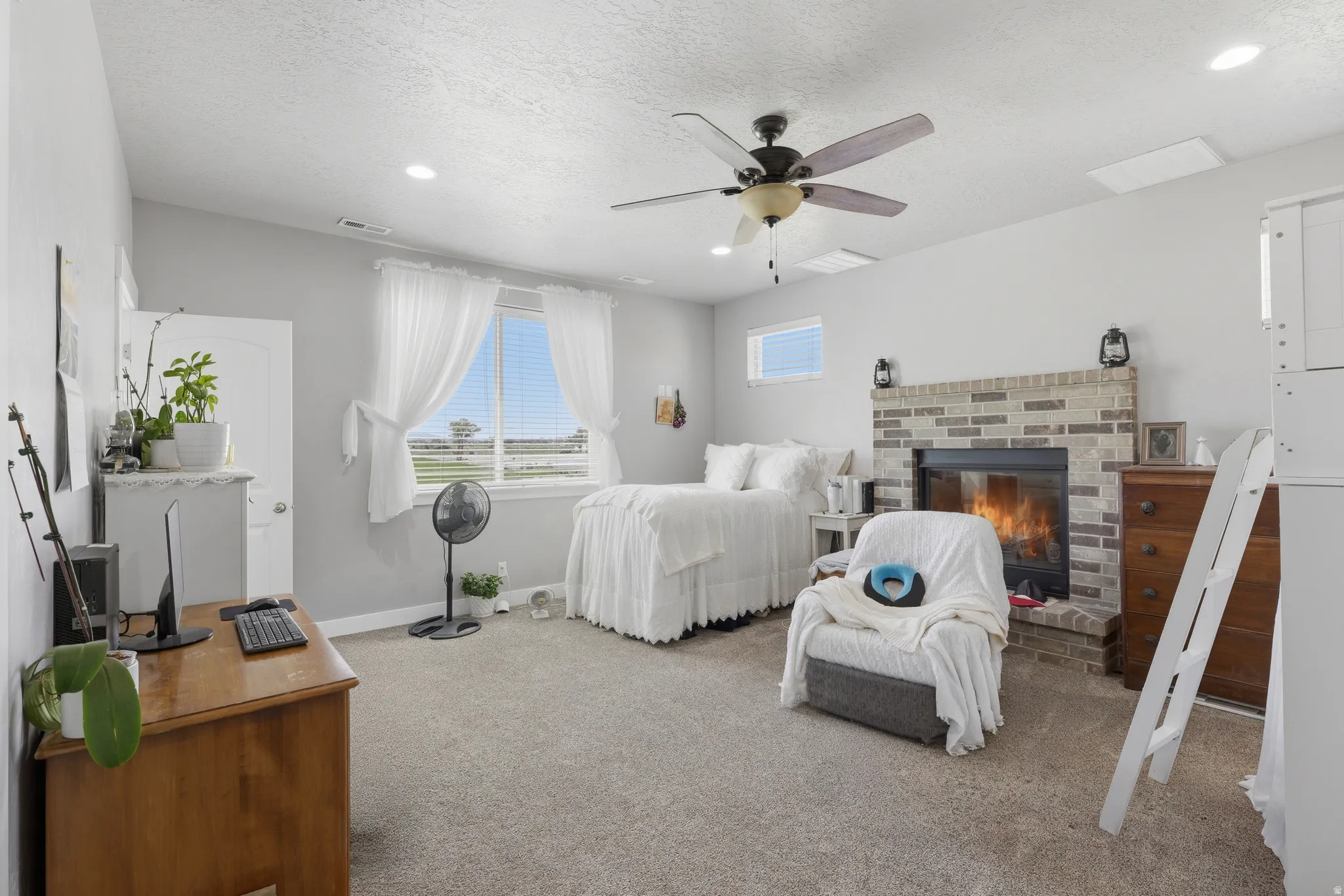 Master bedroom. Carpeted room featuring a stone-clad fireplace with a brick hearth, a ceiling fan, and multiple windows