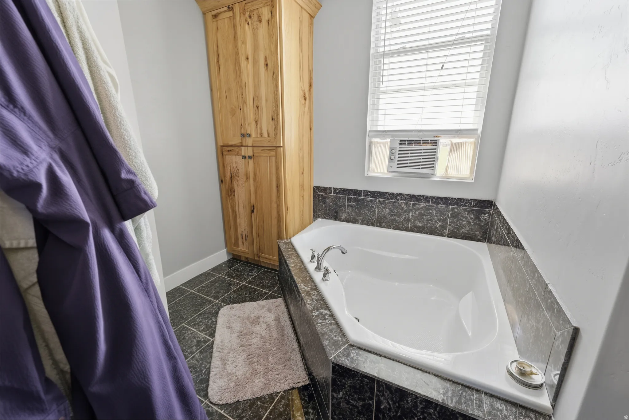Master bathroom- Corner soaking tub with a tiled surround, wood-finish cabinetry, and dark tiled flooring