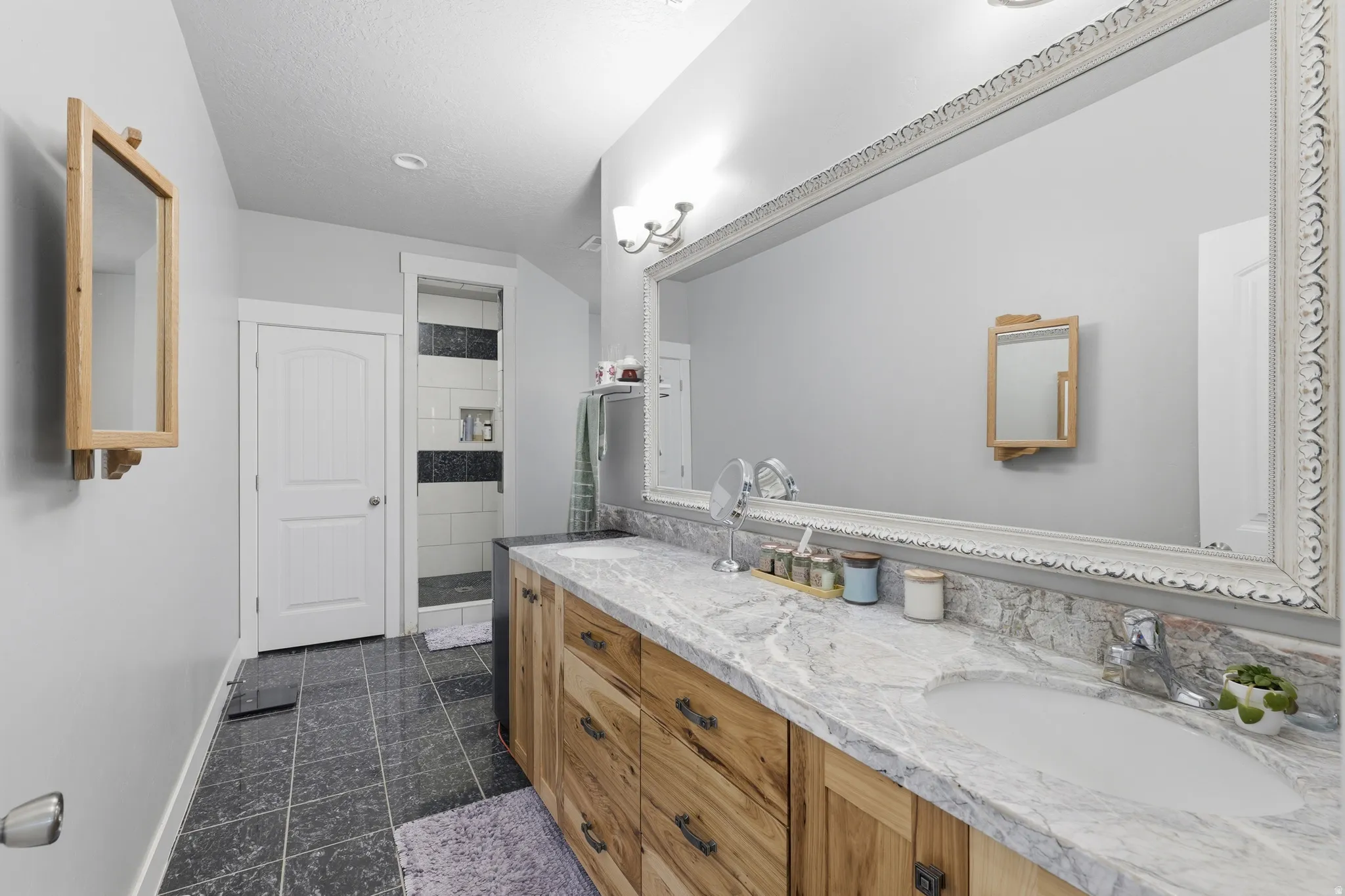 Master Bathroom- Spacious bathroom featuring a dual vanity with light wood-finish cabinetry, a large framed mirror, and a walk-in shower with tiled walls