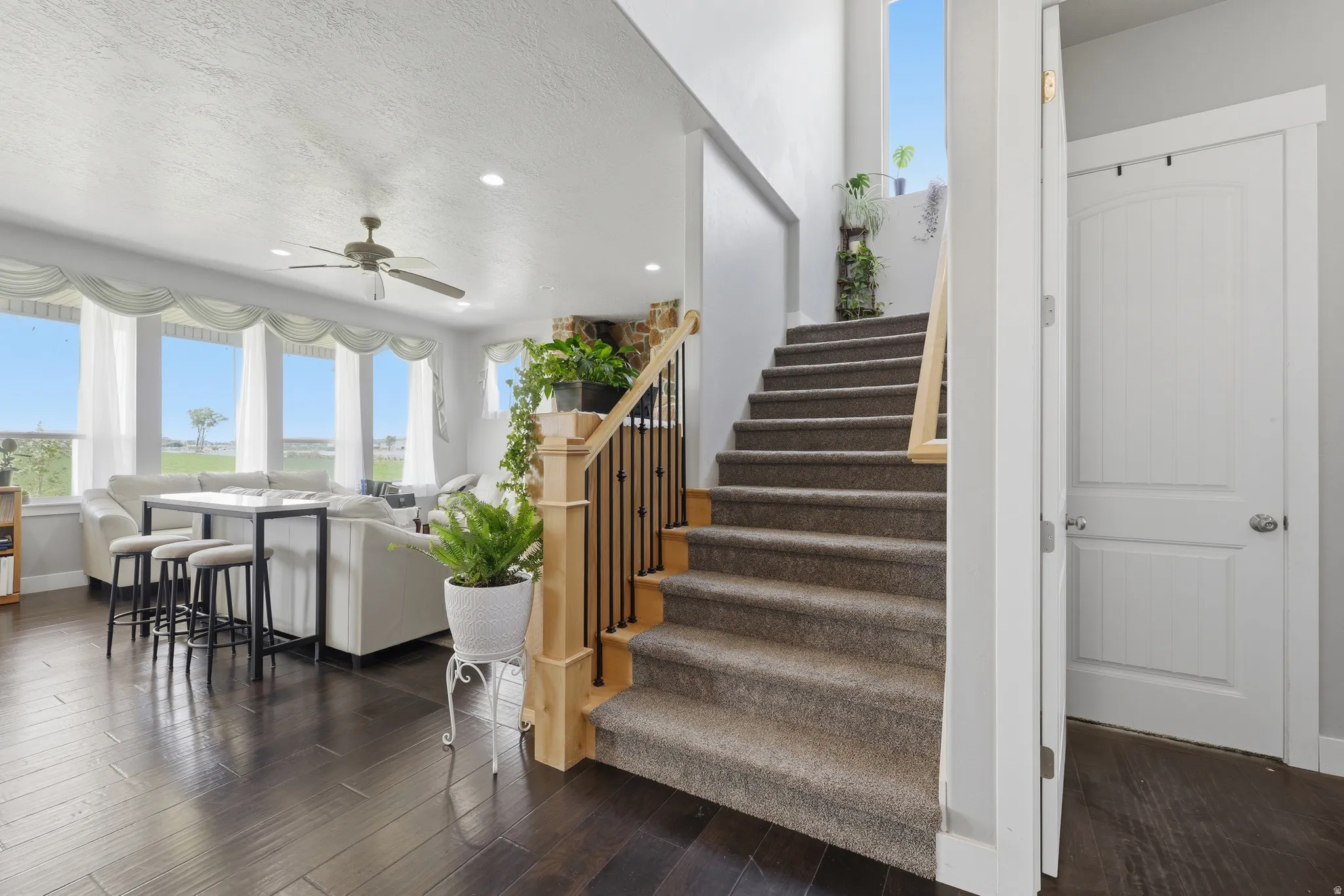 Spacious interior featuring a carpeted staircase with wood and wrought iron railing, dark wood-finish flooring, recessed lighting, and a ceiling fan