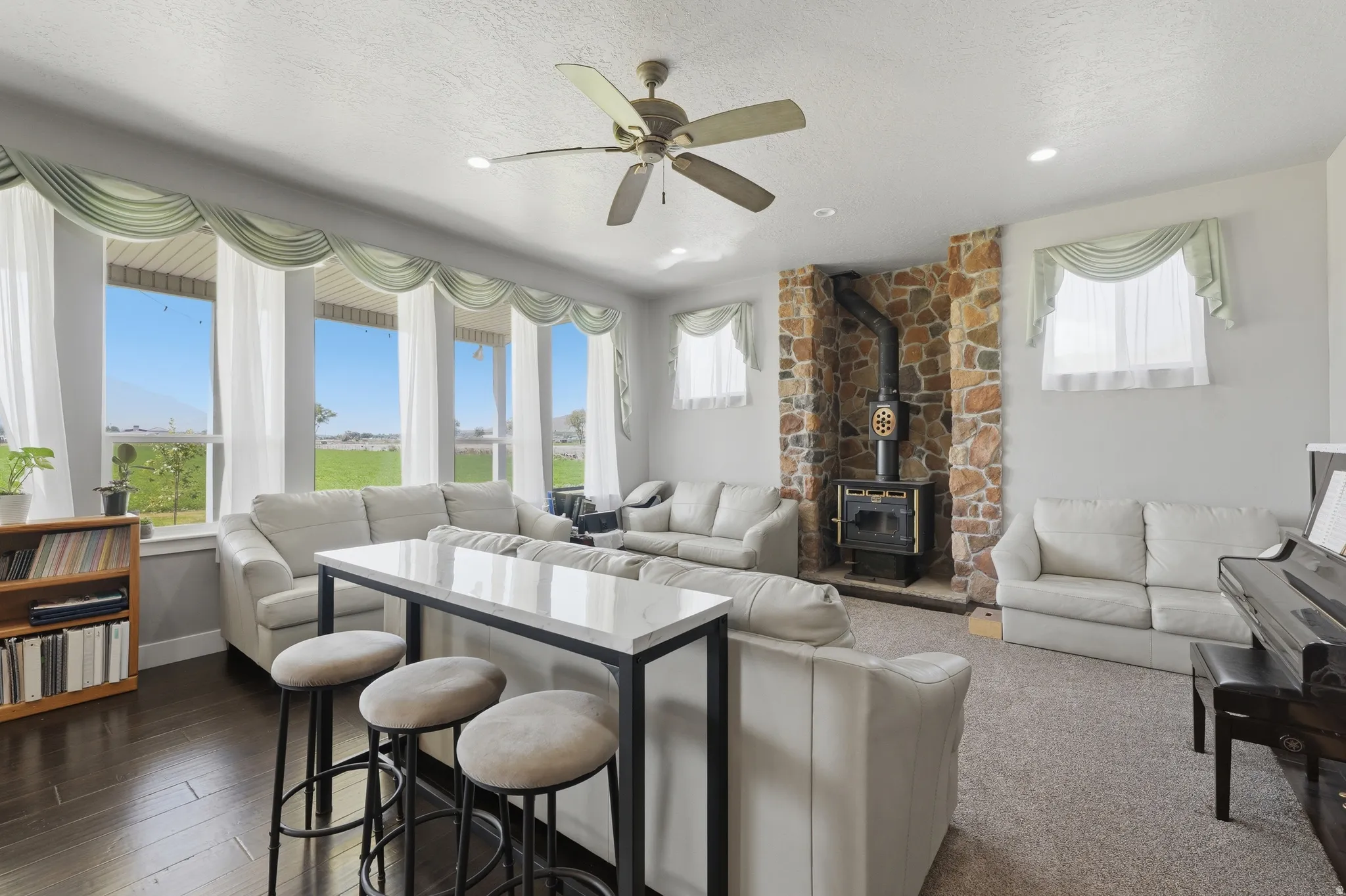 Spacious living area featuring a stone accent wall with a wood-burning stove, dark wood-finish flooring, and recessed lighting