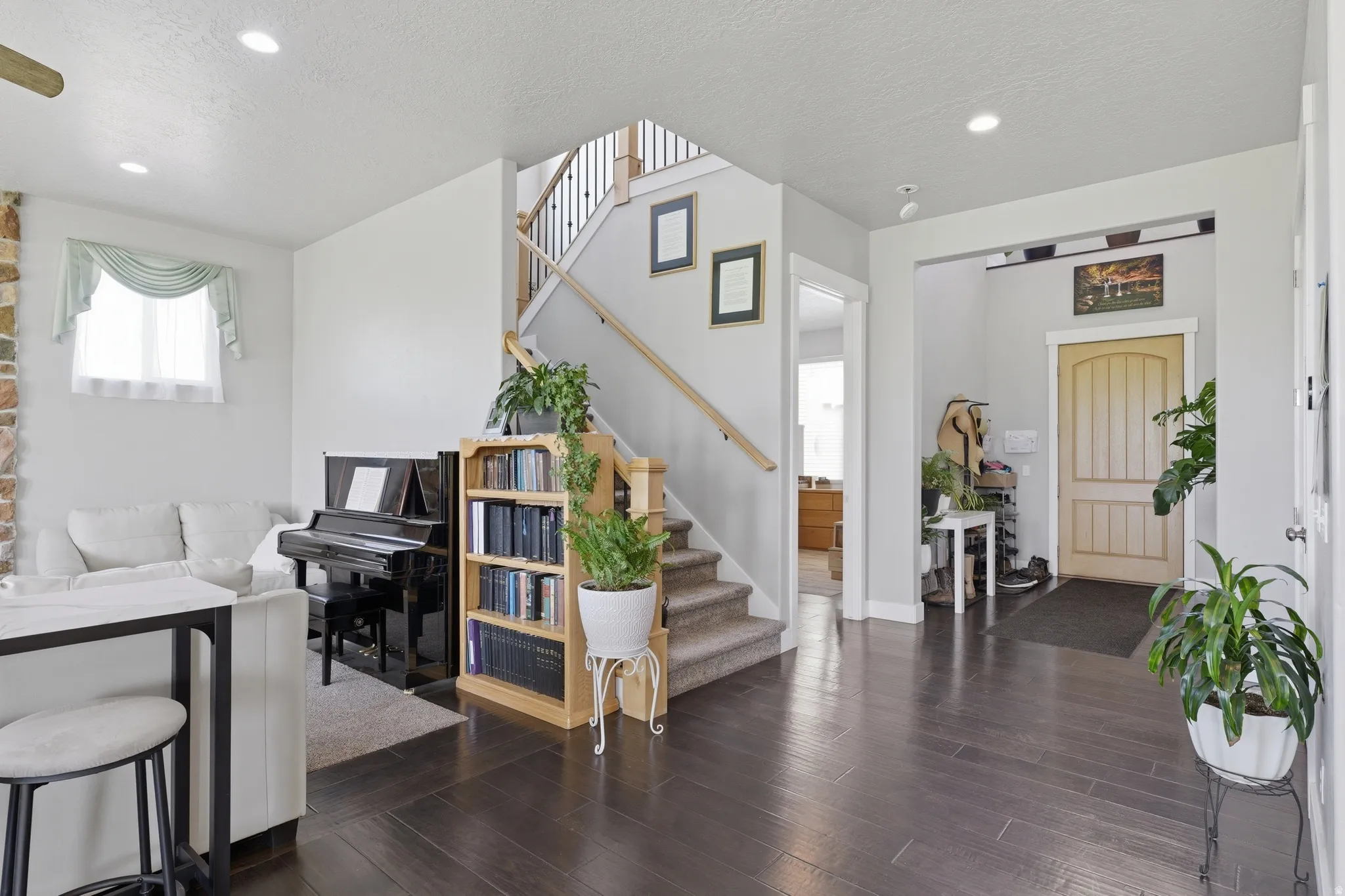Main living area featuring dark wood-finish flooring, recessed lighting, a staircase with carpeted treads, and a light-colored paneled entry door