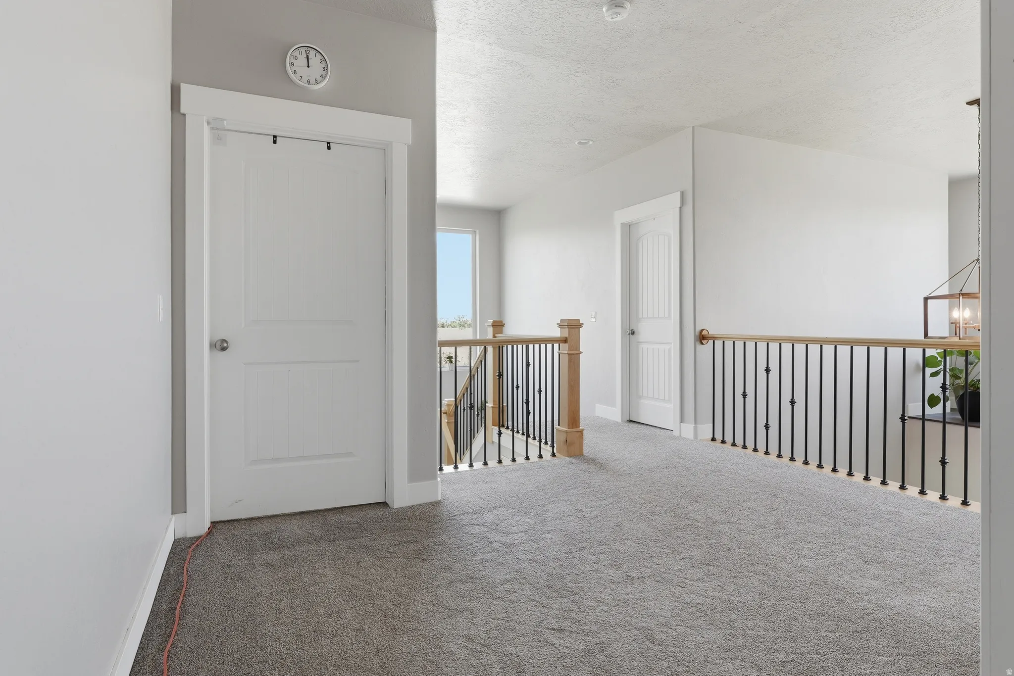 Carpeted upper-level hallway featuring a railing with wood handrails and black metal spindles