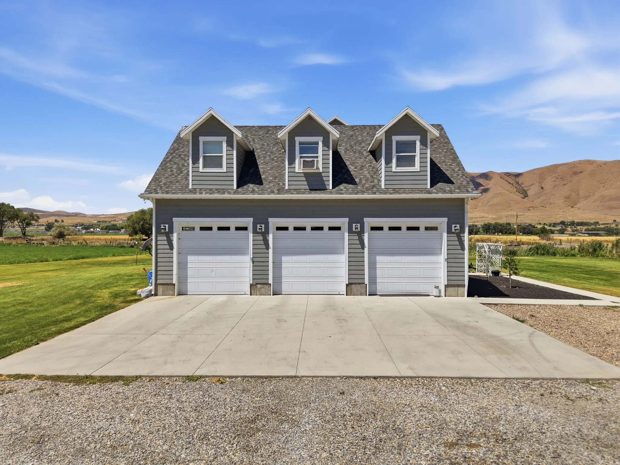 Three-car detached garage structure featuring gray siding, a shingled roof, and three dormer windows