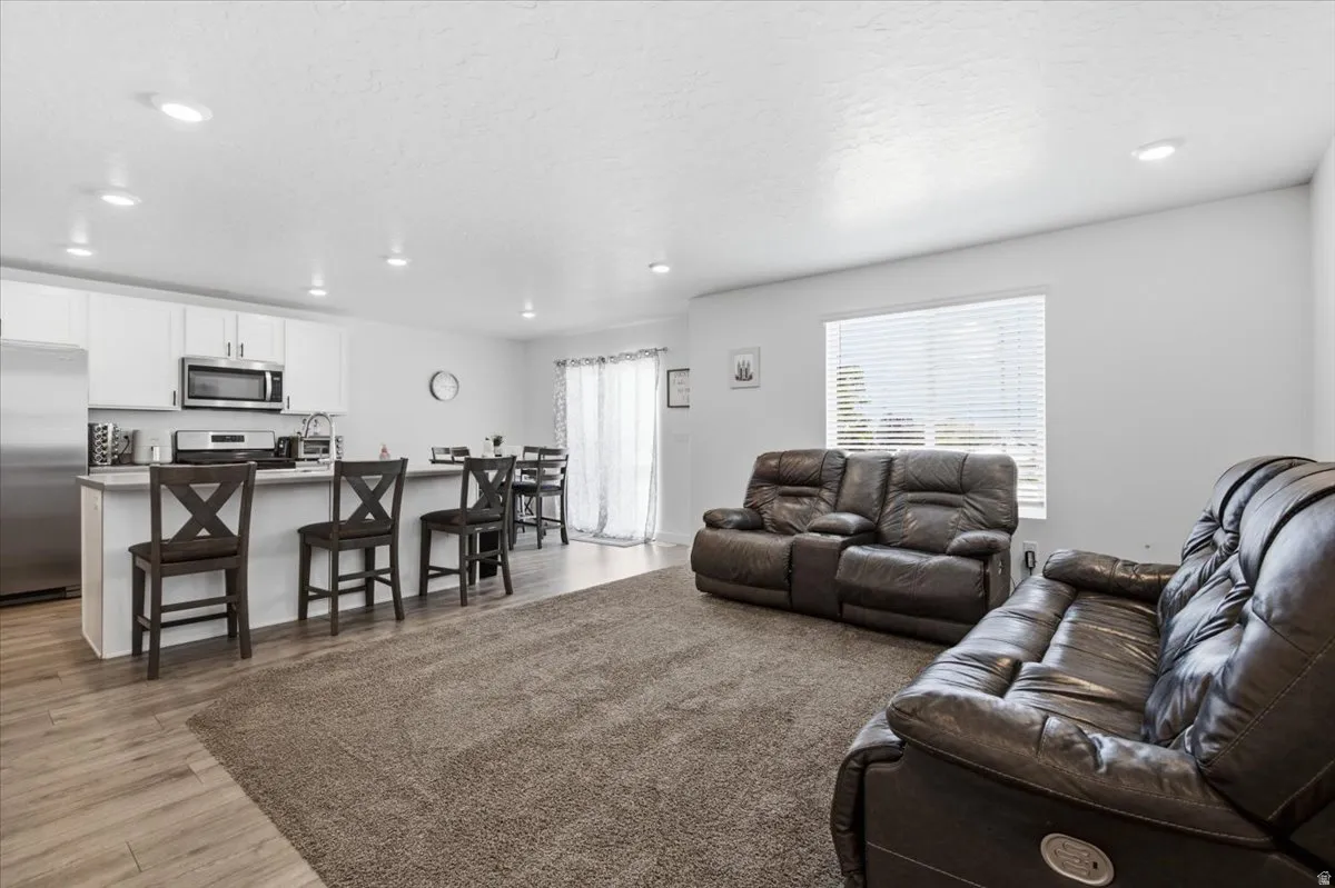 Open-concept living area featuring a kitchen with white cabinetry and stainless steel appliances, a breakfast bar, recessed lighting, and wood-finish flooring