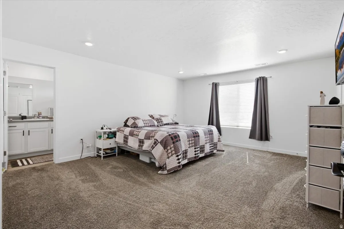 Carpeted bedroom with recessed lighting and a window featuring horizontal blinds