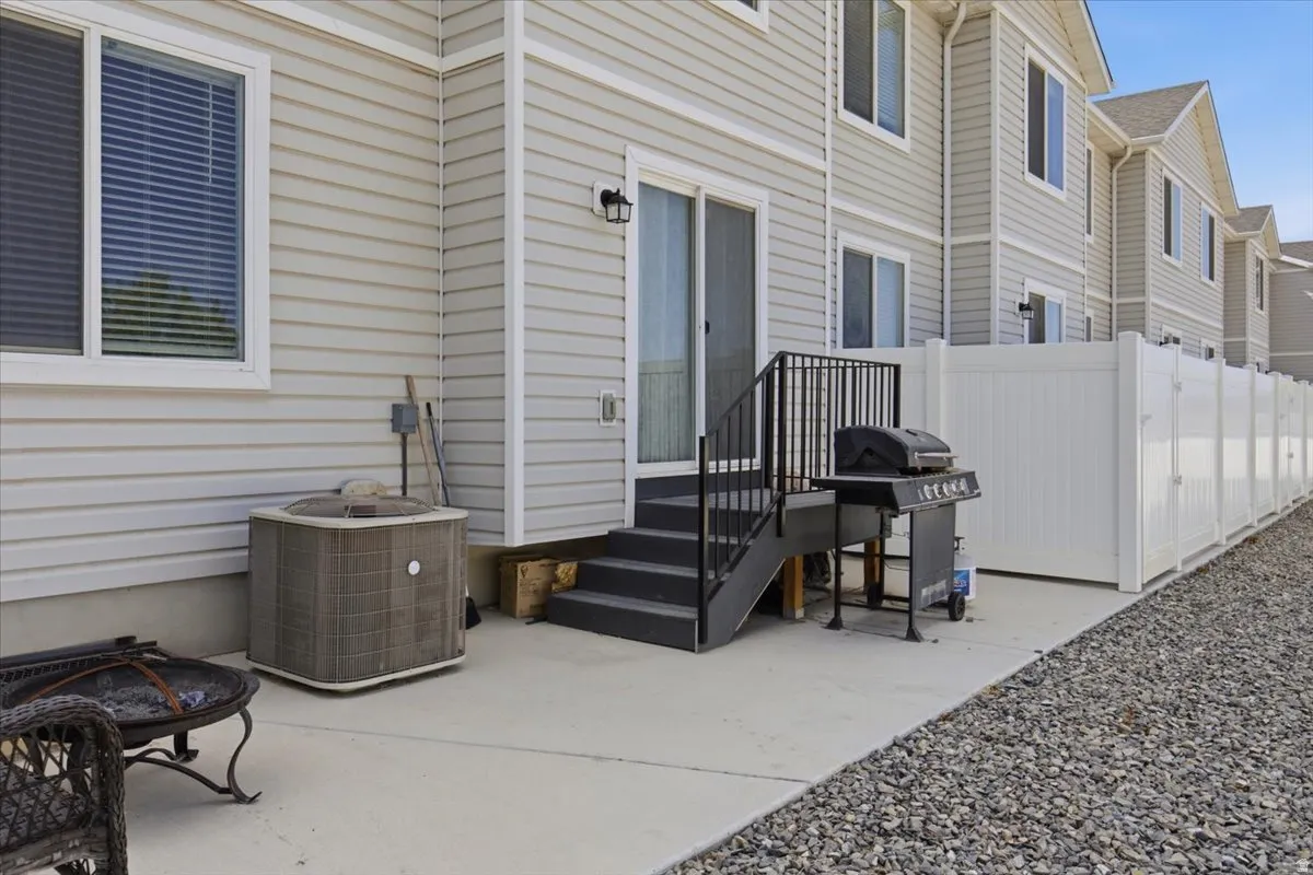 Rear exterior featuring light-colored siding, a concrete patio, a sliding glass door, a black outdoor staircase with railing, and a white privacy fence