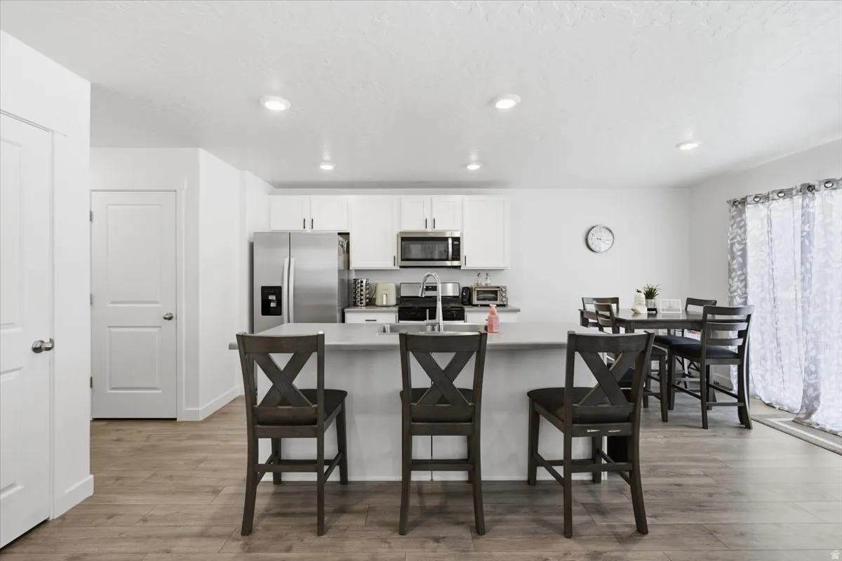 Kitchen featuring a central island with countertop seating, stainless steel appliances, white cabinetry, and wood-finish flooring