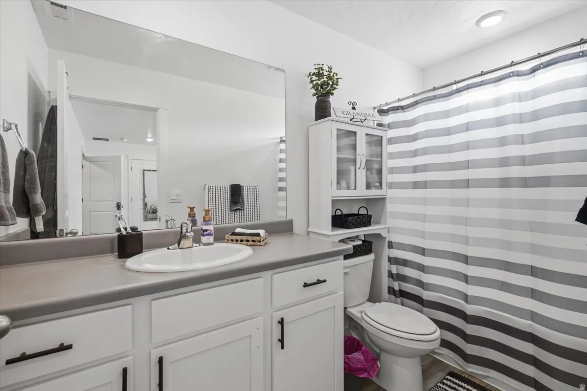 Bathroom featuring a white vanity with a gray countertop, an oval undermount sink, a large wall-mounted mirror, and a white toilet with an over-the-toilet storage cabinet
