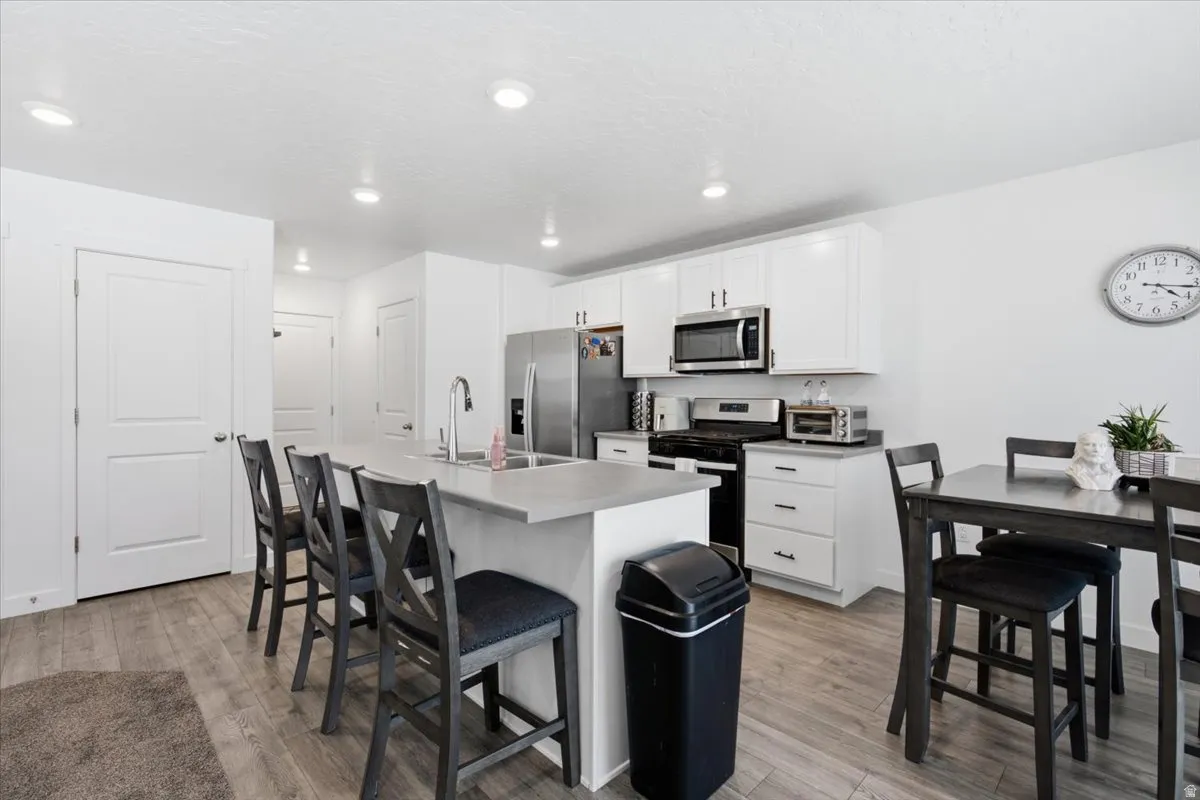 Modern kitchen featuring white cabinetry, stainless steel appliances, a large island with sink, ample counter space, and wood-finish flooring