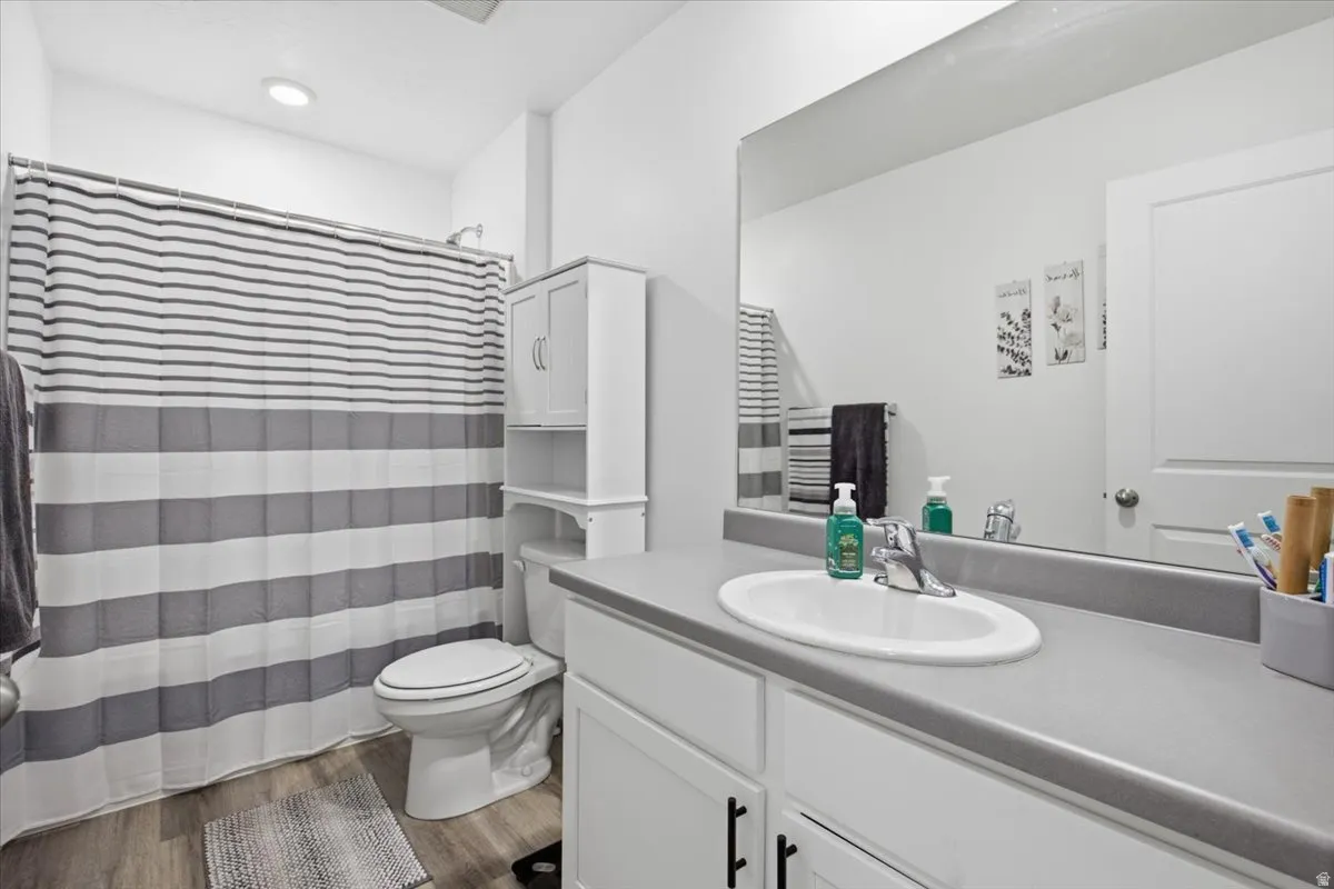 Bathroom featuring an oval undermount sink set in a gray countertop, white vanity cabinetry with dark hardware, a spacious mirror, and wood-finish flooring