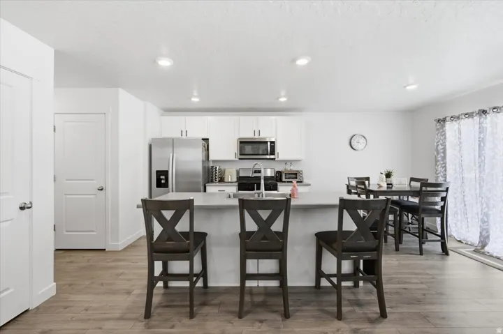 Kitchen featuring a central island with countertop seating, stainless steel appliances, white cabinetry, and wood-finish flooring