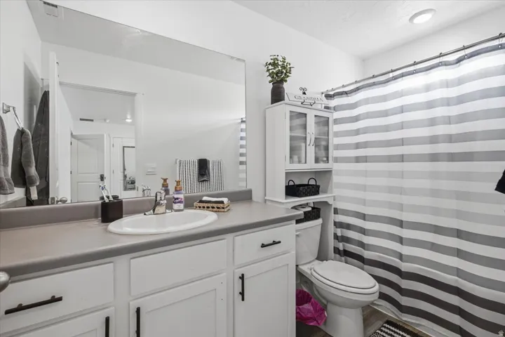 Bathroom featuring a white vanity with a gray countertop, an oval undermount sink, a large wall-mounted mirror, and a white toilet with an over-the-toilet storage cabinet