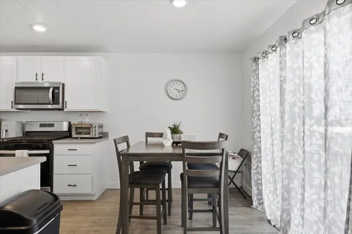 Kitchen and dining area featuring white cabinetry, stainless steel appliances, and wood-finish flooring