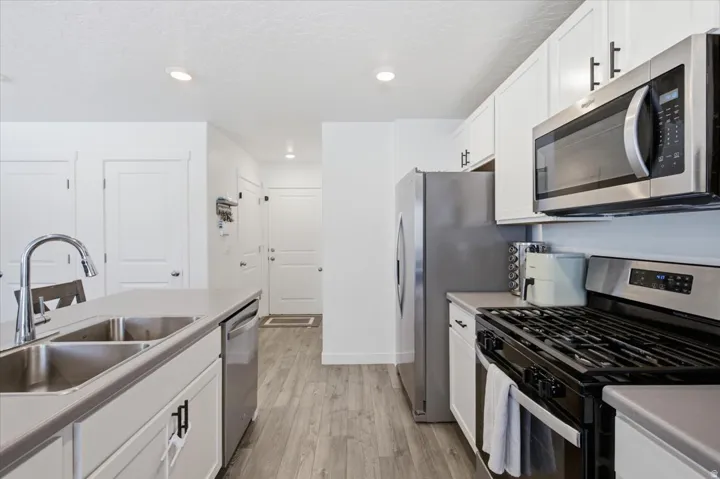 Modern kitchen featuring light wood-finish flooring, white cabinetry with black hardware, stainless steel appliances, and a double basin sink with a high-arc faucet