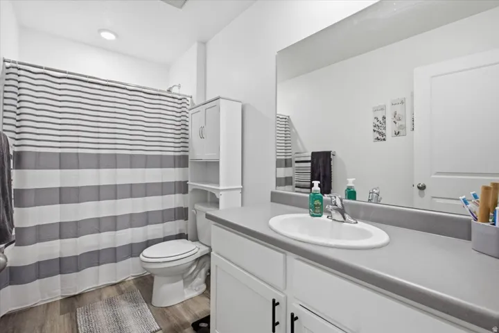 Bathroom featuring an oval undermount sink set in a gray countertop, white vanity cabinetry with dark hardware, a spacious mirror, and wood-finish flooring