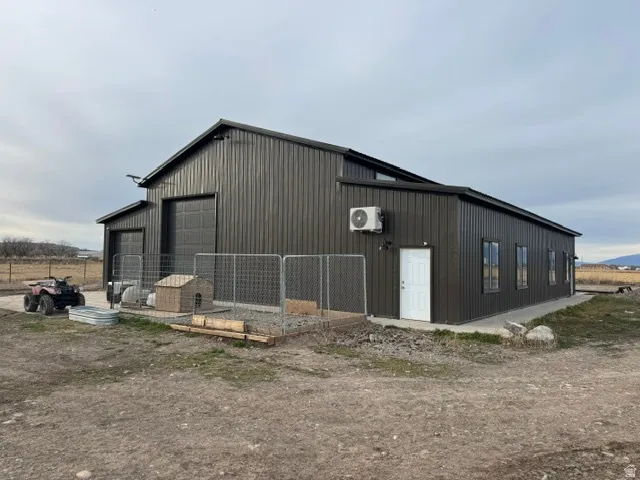 Metal-sided outbuilding featuring two large garage doors, multiple exterior windows, a white entry door, and an attached mini-split HVAC unit