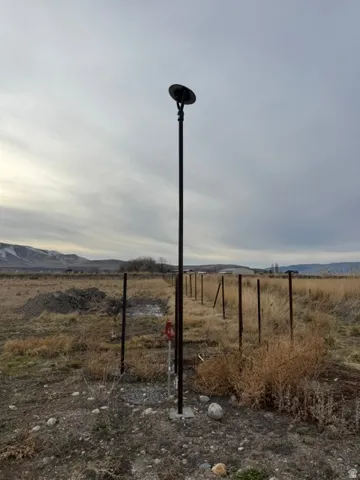 Utility pole with an attached street light fixture, established fencing, and visible mountain backdrop