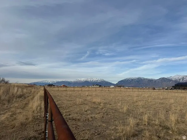 Expansive undeveloped land featuring a rustic metal fence, natural grass and brush, and distant snow-capped mountains