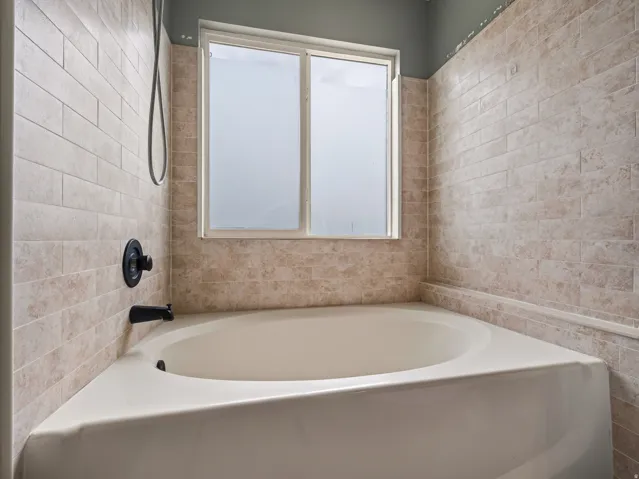 Corner soaking tub featuring matte black fixtures, tile surround, and a frosted window